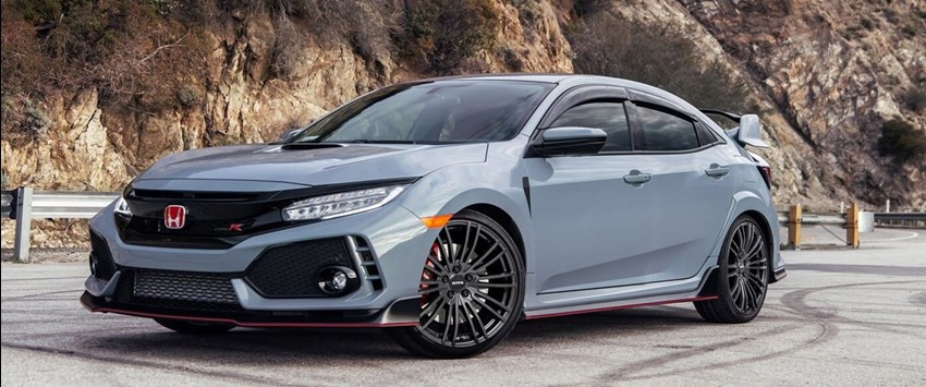 En sportig grå Honda Civic Type R står parkerad på en bergsväg med klippor i bakgrunden. Bilen har en aggressiv frontdesign, stora svarta lättmetallfälgar och en bakvinge för extra aerodynamik.