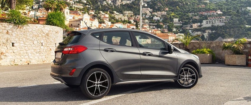 Grå Ford Fiesta med svarta lättmetallfälgar parkerad med utsikt över en kuststad med sluttande bebyggelse i bakgrunden.