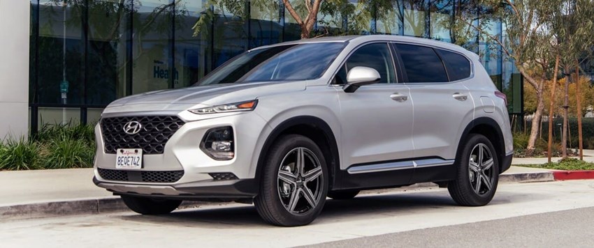 Silverfärgad Hyundai SUV parkerad vid trottoar framför en modern glasbyggnad, med sportiga femekrade lättmetallfälgar.