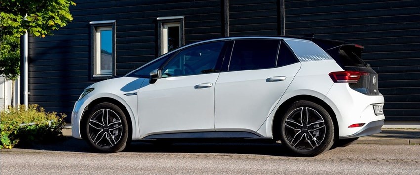 En vit Volkswagen ID.3 elbil står parkerad vid en trottoar framför en mörk träfasad. Bilen är utrustad med IMAGE Colt lättmetallfälgar i tvåtonad svart och silver finish.
